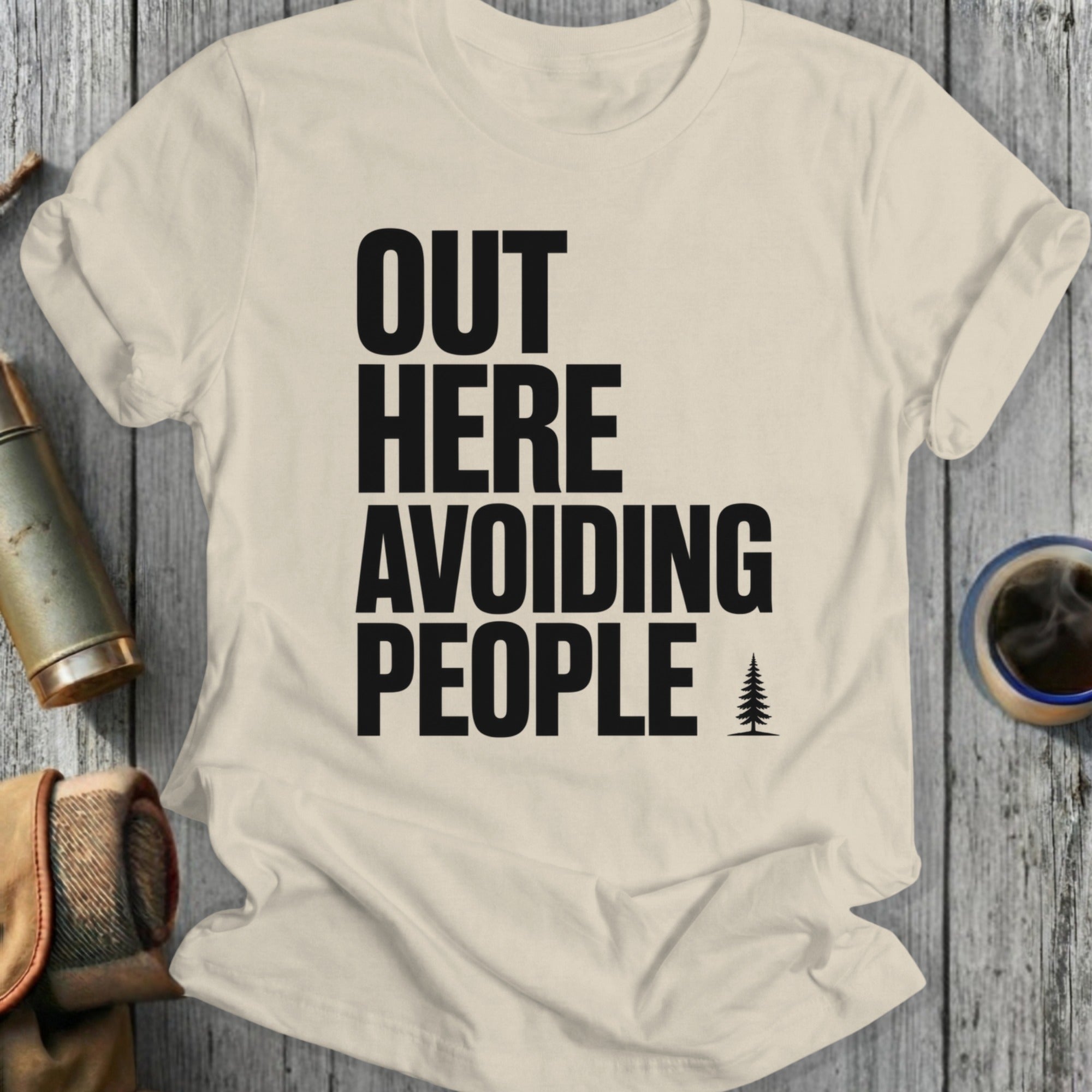 T-shirt with black text "OUT HERE AVOIDING PEOPLE" and a small tree graphic.