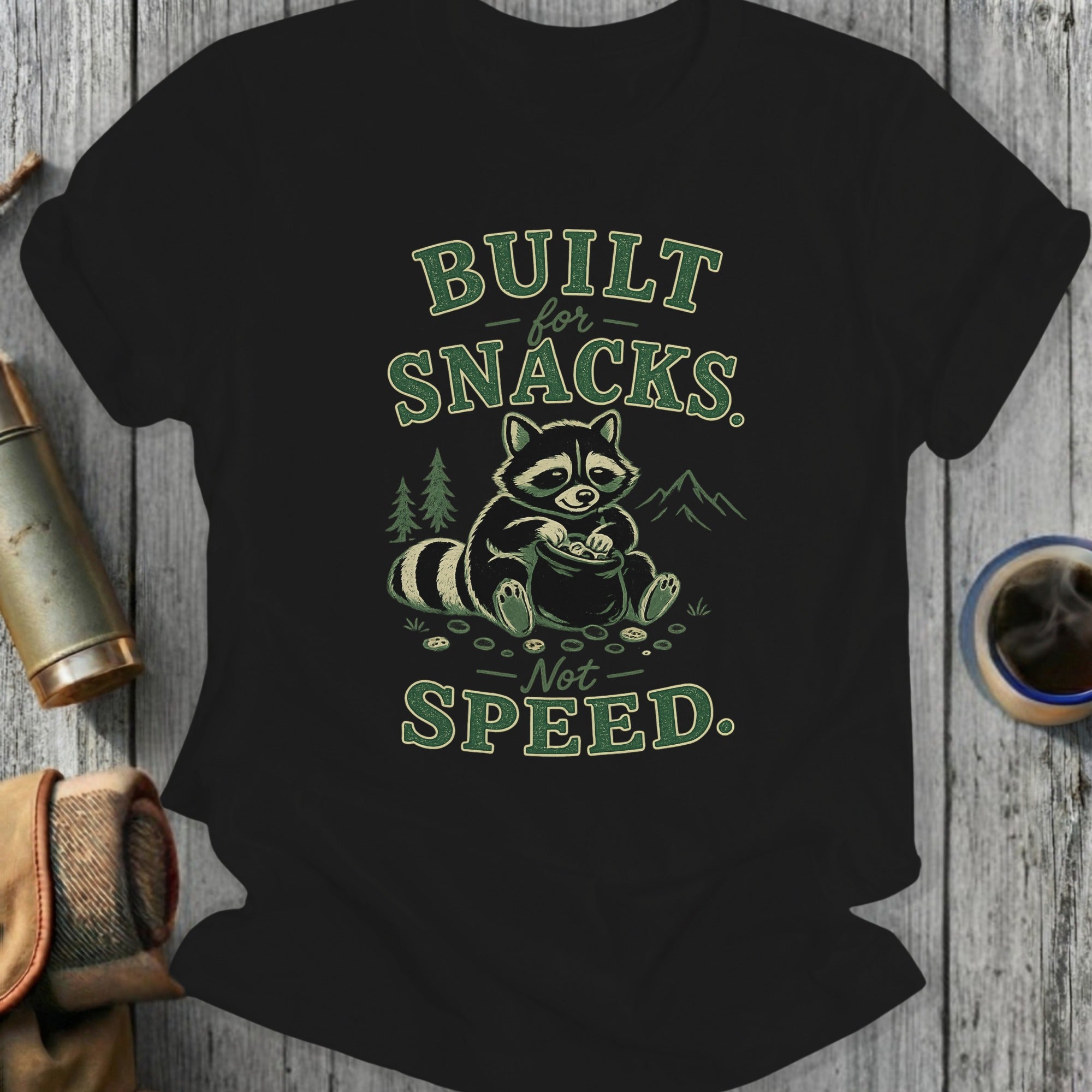 T-shirt with raccoon sitting by a pile of snacks, text reads "BUILT for SNACKS. Not SPEED."