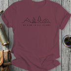 Maroon t-shirt with a line drawing of mountains, campfire, and tent above text "BE KIND TO ALL CLIMBS".