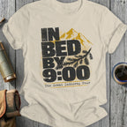 Cream t-shirt with distressed text and mountain graphic that reads "IN BED BY 9:00 The Great Indoorsy Tour."