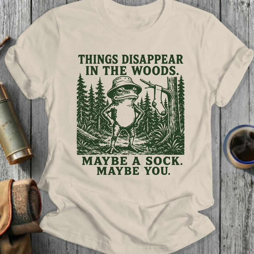 Frog in bucket hat standing in woods with text "Things disappear in the woods. Maybe a sock. Maybe you."