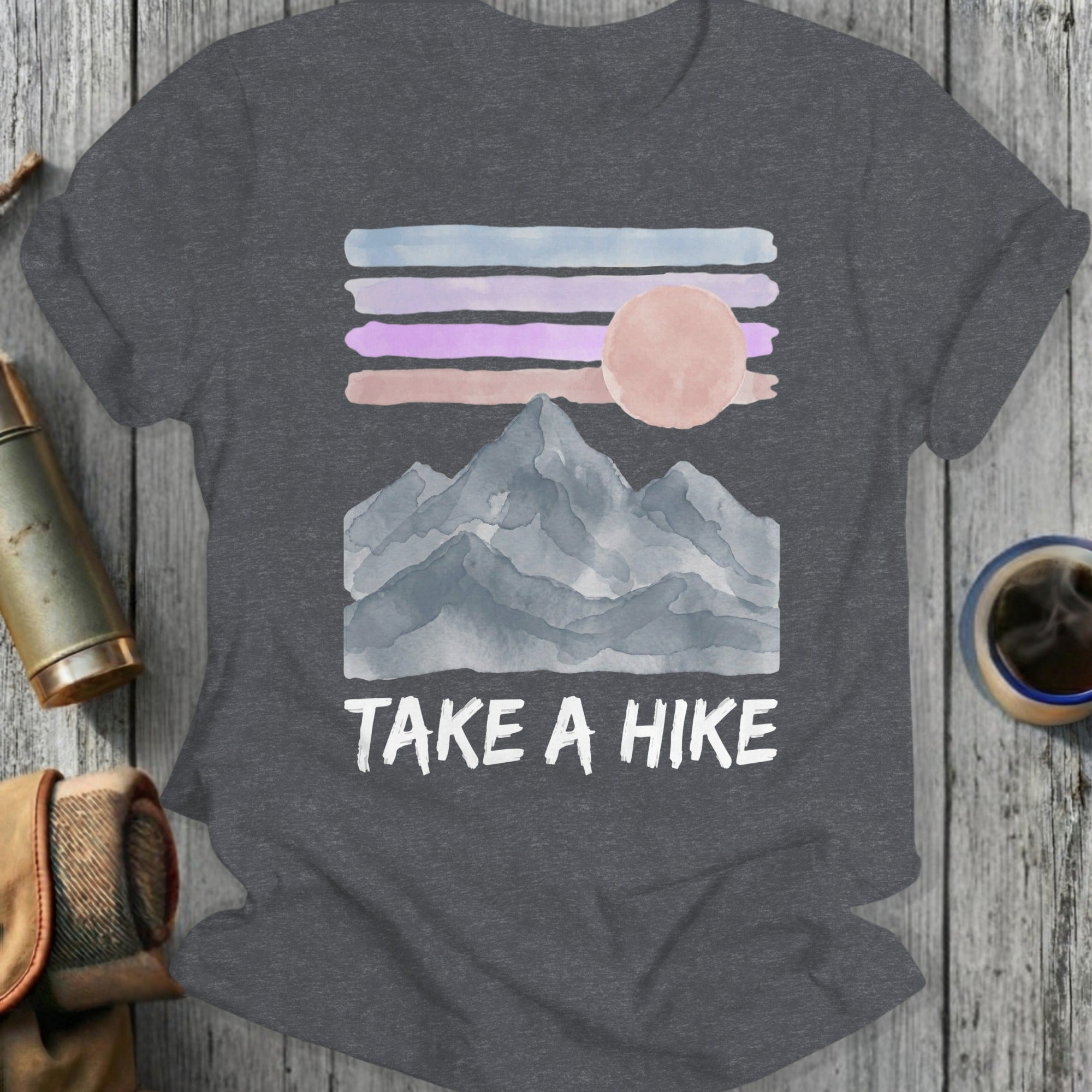 Dark gray t-shirt with watercolor mountains, striped sky, sun, and "TAKE A HIKE" text.