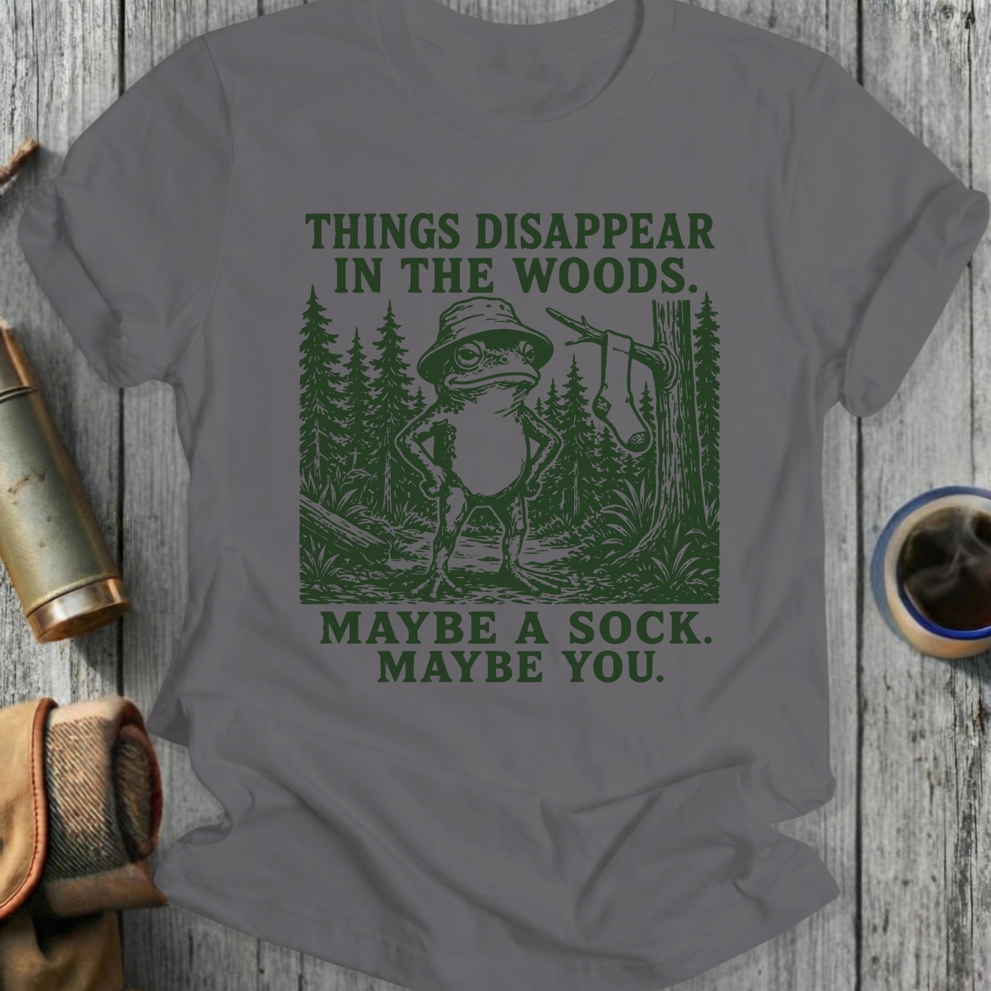 Gray t-shirt with forest graphic and text "THINGS DISAPPEAR IN THE WOODS. MAYBE A SOCK. MAYBE YOU."