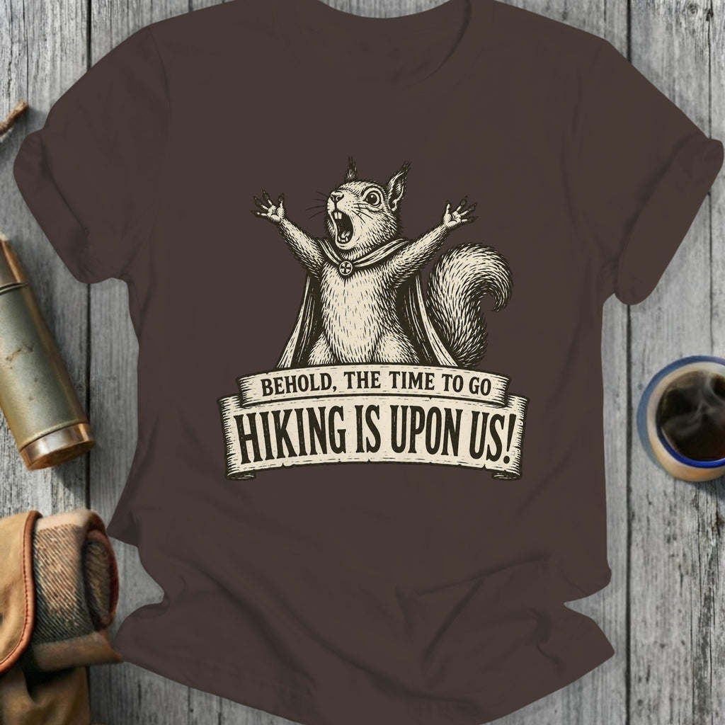 Brown t-shirt with a vintage-style drawing of a squirrel and the text "BEHOLD, THE TIME TO GO HIKING IS UPON US!"