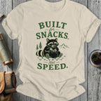 T-shirt with raccoon collecting snacks, text reads "BUILT for SNACKS - Not SPEED."