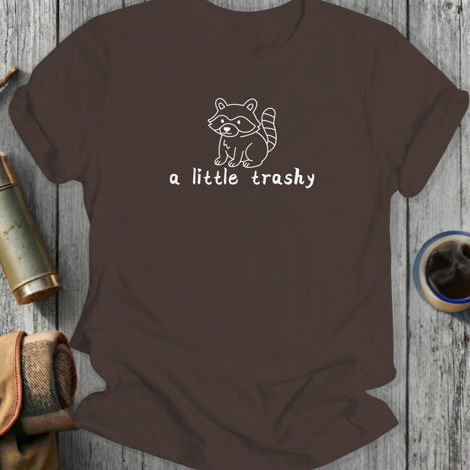 Brown t-shirt with white outline of a raccoon and text "a little trashy".