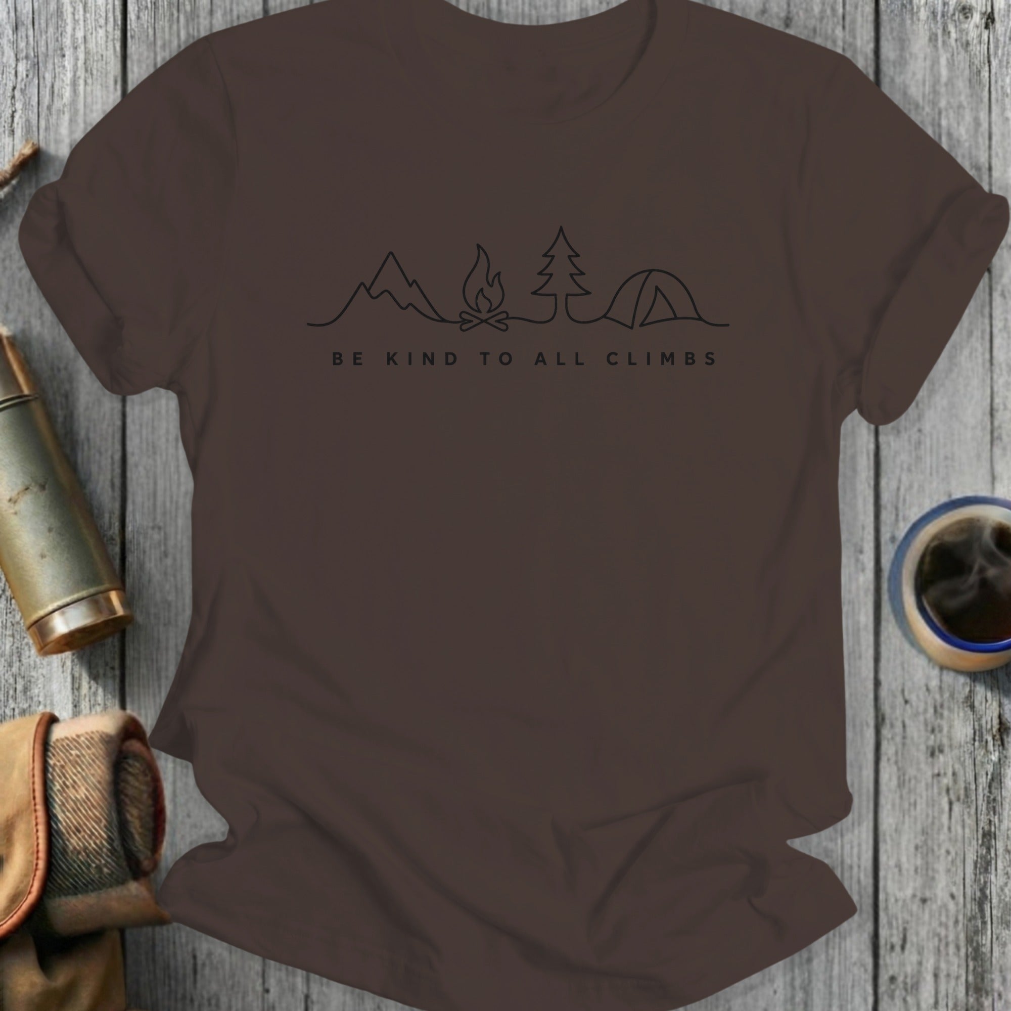 Brown t-shirt with line drawing of mountains, campfire, tree, and tent, and text "BE KIND TO ALL CLIMBS".