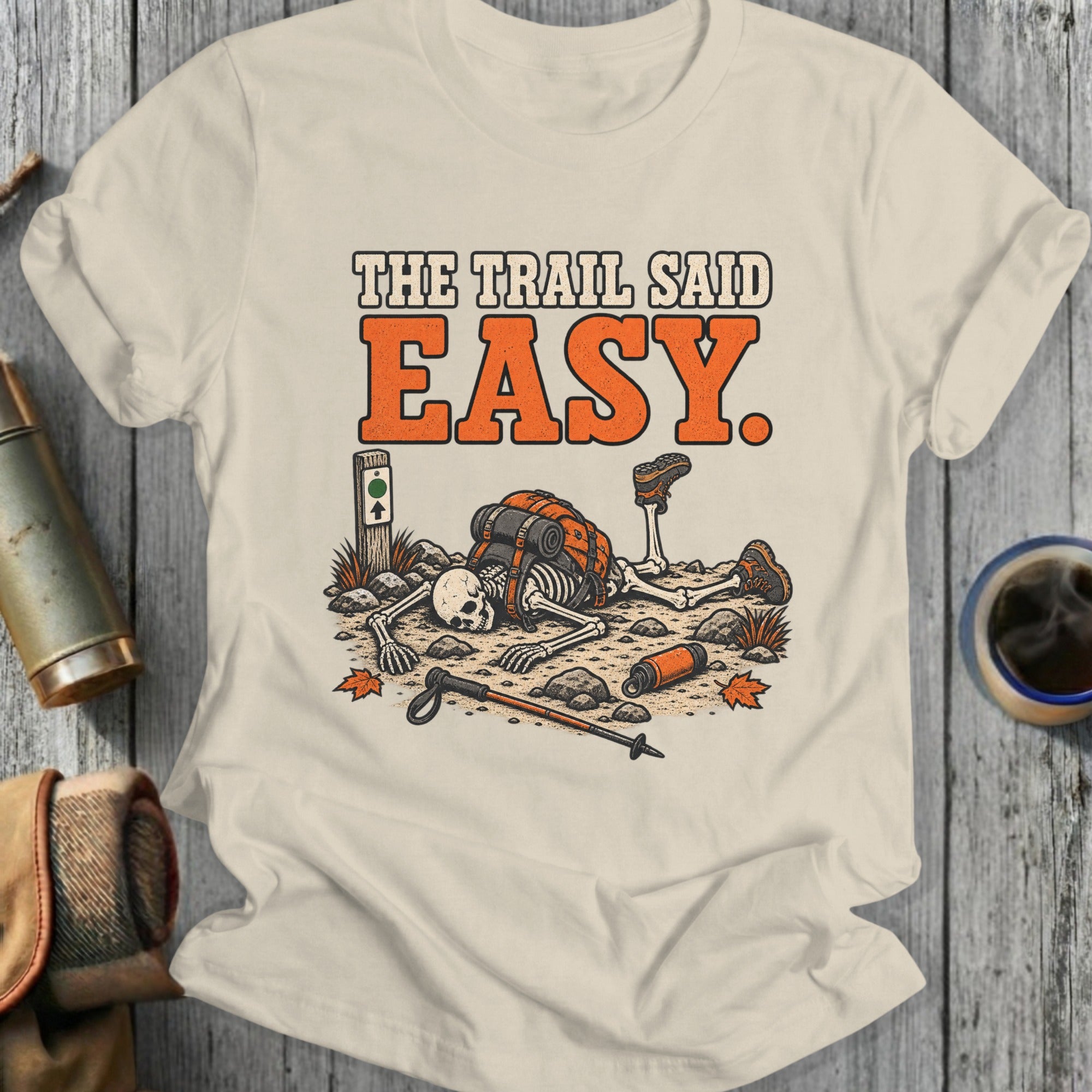 Skeleton hiker with backpack lies on ground with text "THE TRAIL SAID EASY".