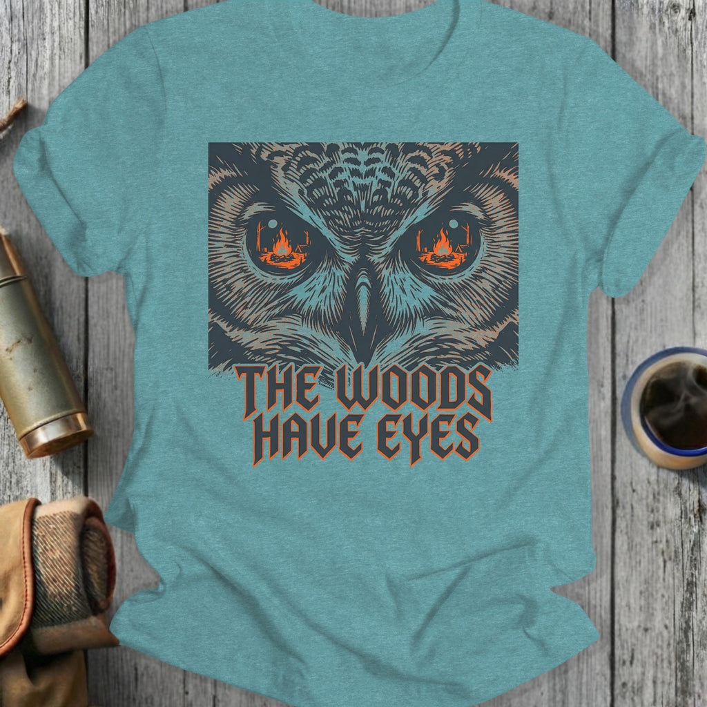 T-shirt graphic featuring owl eyes with fire and text "THE WOODS HAVE EYES".