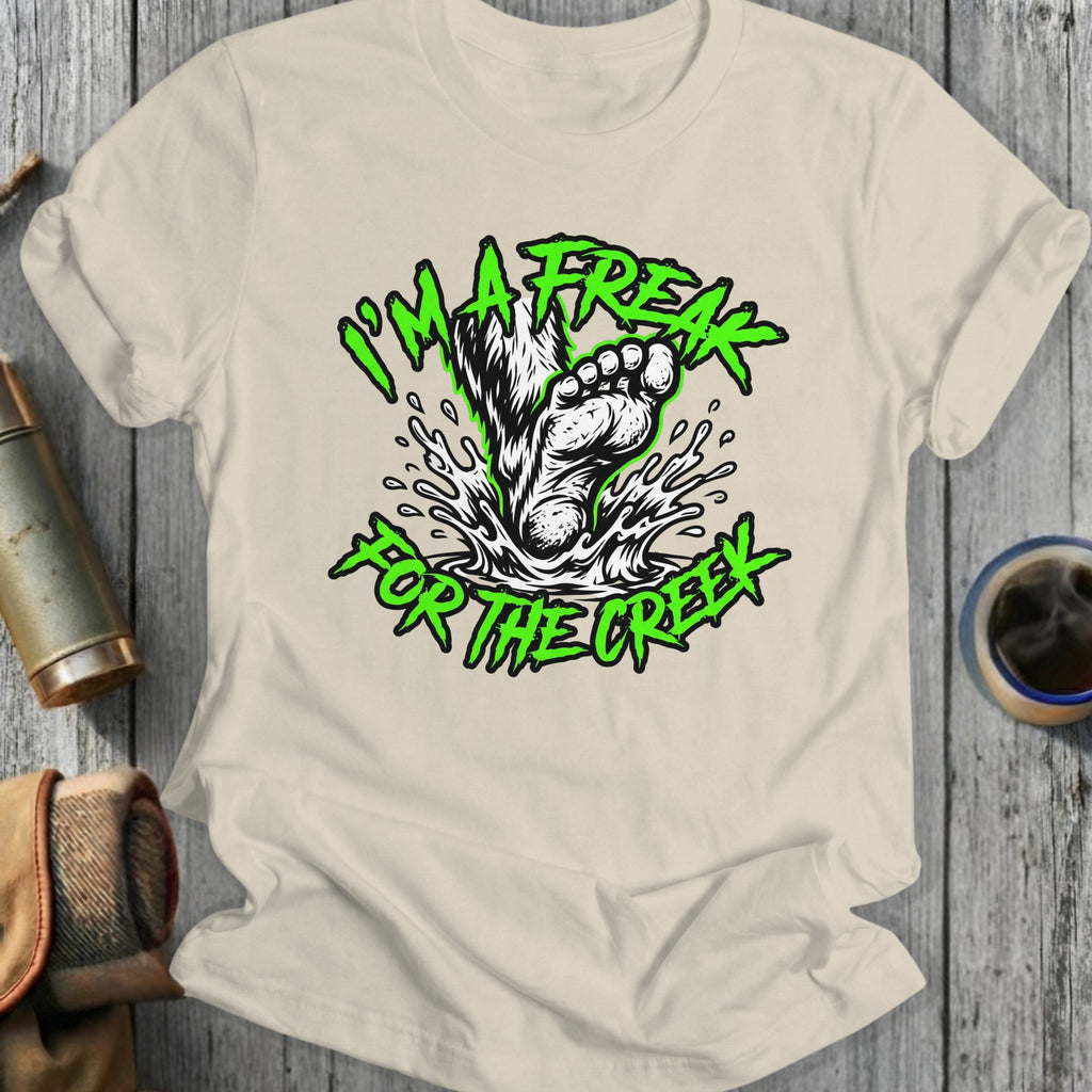 Green text and Bigfoot foot splashing water on cream t-shirt.