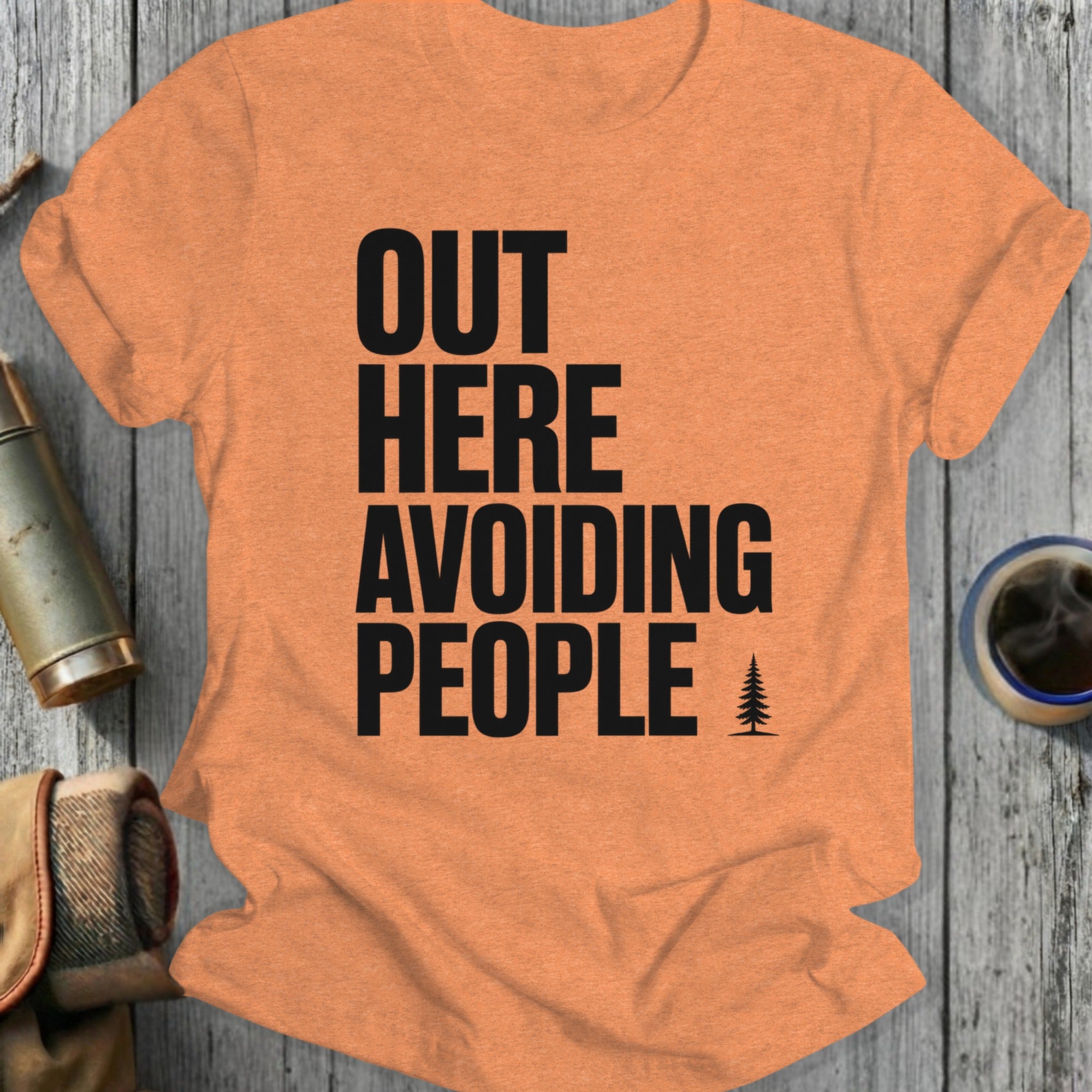 Orange t-shirt with black text "OUT HERE AVOIDING PEOPLE" and a pine tree.