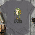 T-shirt with cartoon frog wearing backpack and holding hiking pole, text reads "WE HIKE AT DAWN"