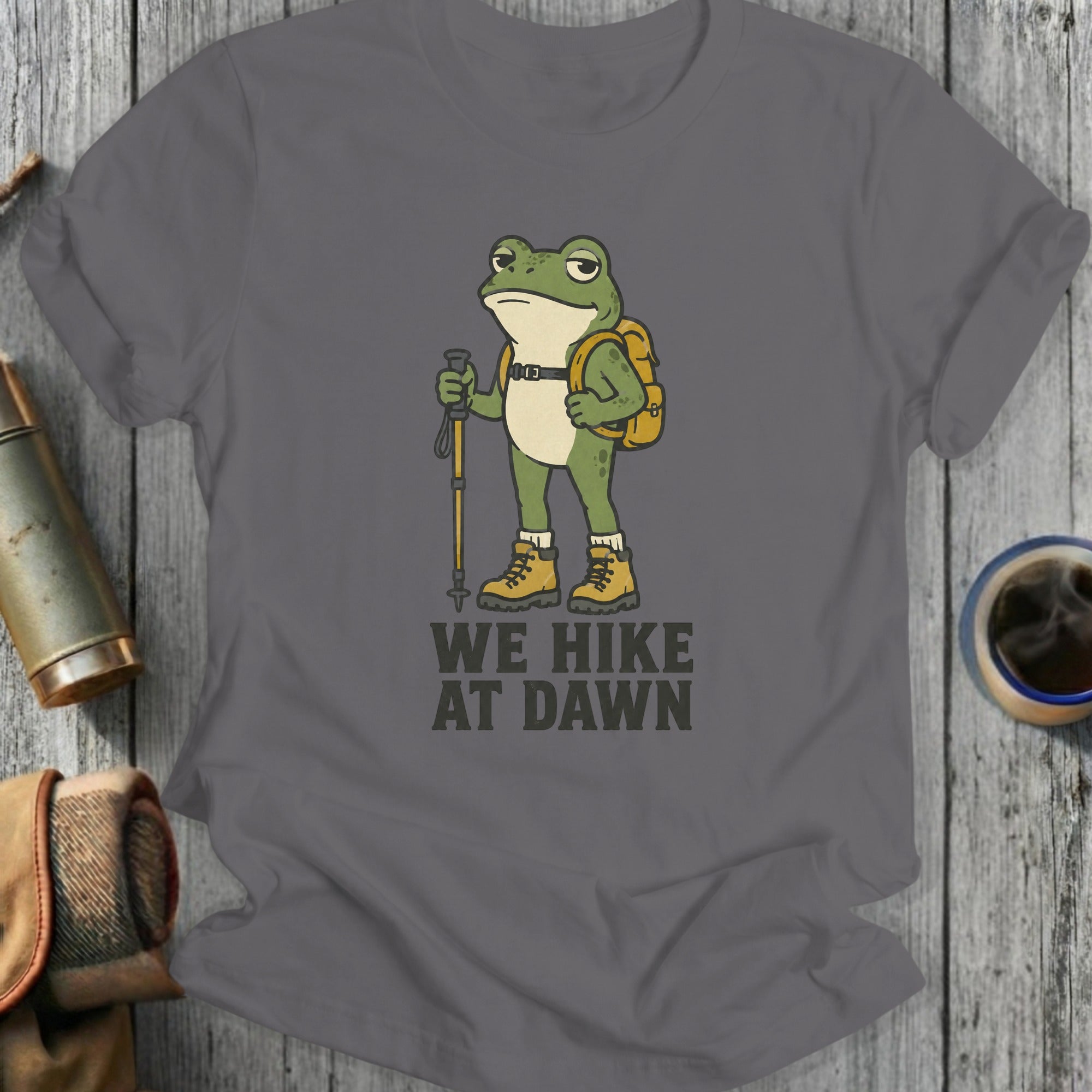 T-shirt with cartoon frog wearing backpack and holding hiking pole, text reads "WE HIKE AT DAWN"