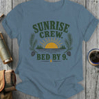 Blue t-shirt with distressed graphic of sunrise over water, text "Sunrise Crew. Bed by 9."