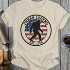 Cream t-shirt with circular "Urban Legend Est. 1776" Bigfoot design and American flag.
