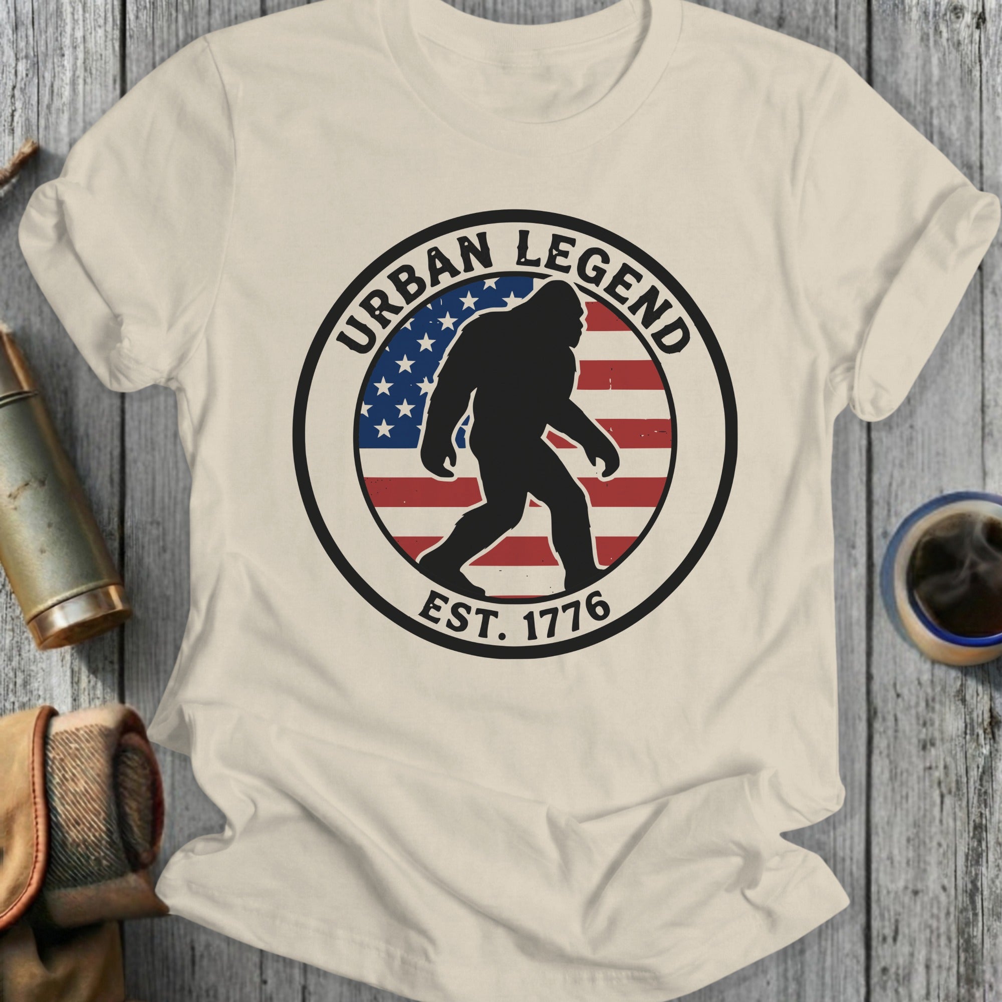 Cream t-shirt with circular "Urban Legend Est. 1776" Bigfoot design and American flag.