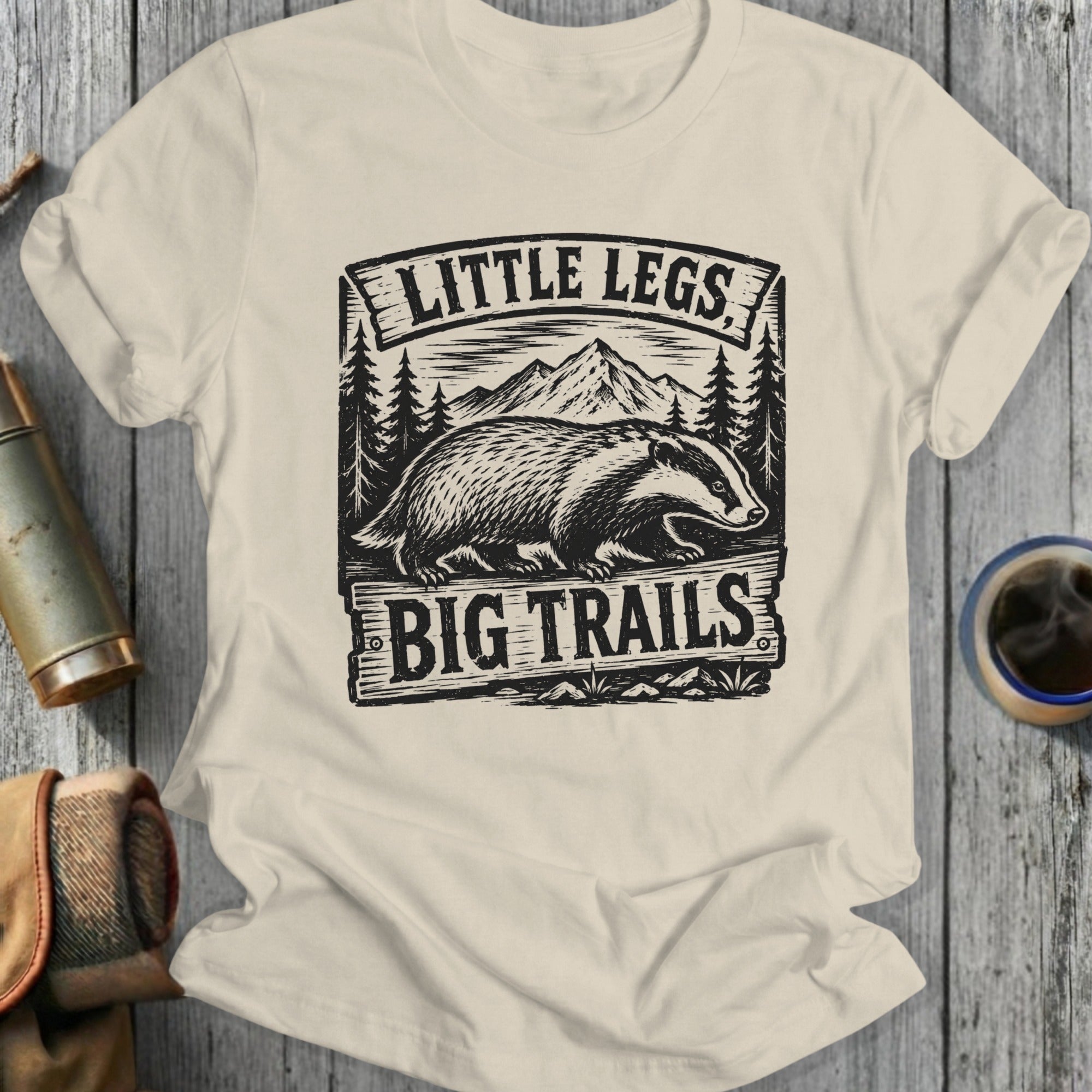Cream t-shirt with badger, mountains, and "Little Legs Big Trails" text.
