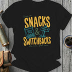 Black t-shirt with "Snacks & Switchbacks" graphic, trail mix bag, and trail sign.