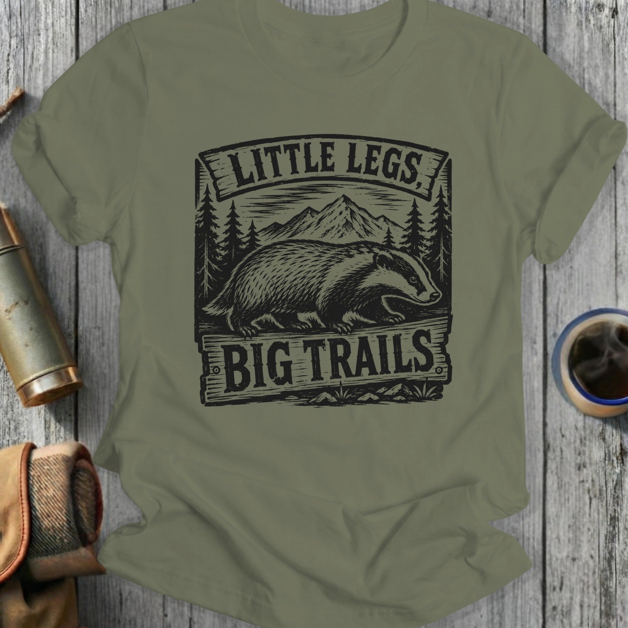 Olive green t-shirt with "Little Legs Big Trails" text and badger illustration.