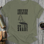 Olive green t-shirt with black text reading "I USED TO SEEK ADVENTURE NOW I SEEK SHADE"