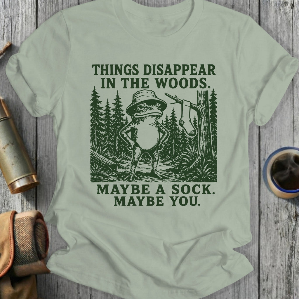 Frog in hat stands in woods with text: Things disappear in the woods. Maybe a sock. Maybe you.