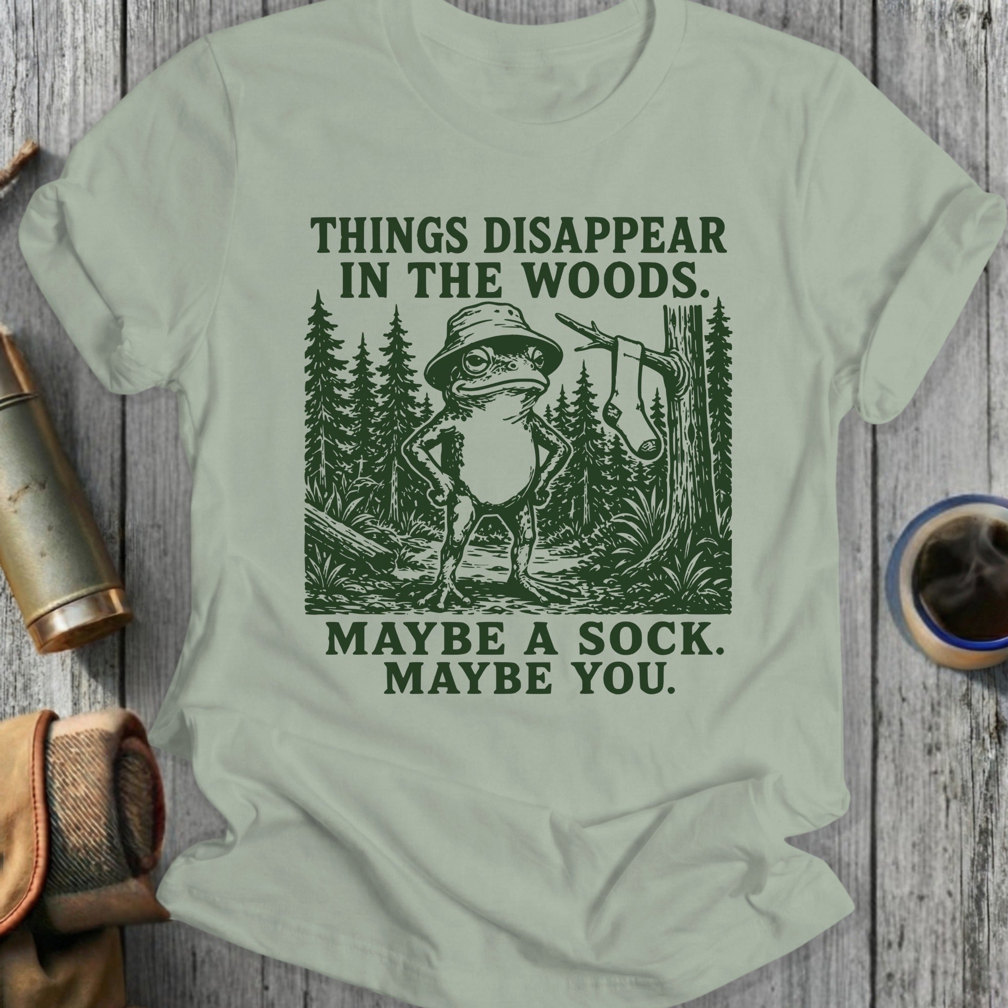 Frog in hat stands in woods with text: Things disappear in the woods. Maybe a sock. Maybe you.