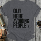 Dark gray t-shirt with "OUT HERE AVOIDING PEOPLE" text and a small tree icon.