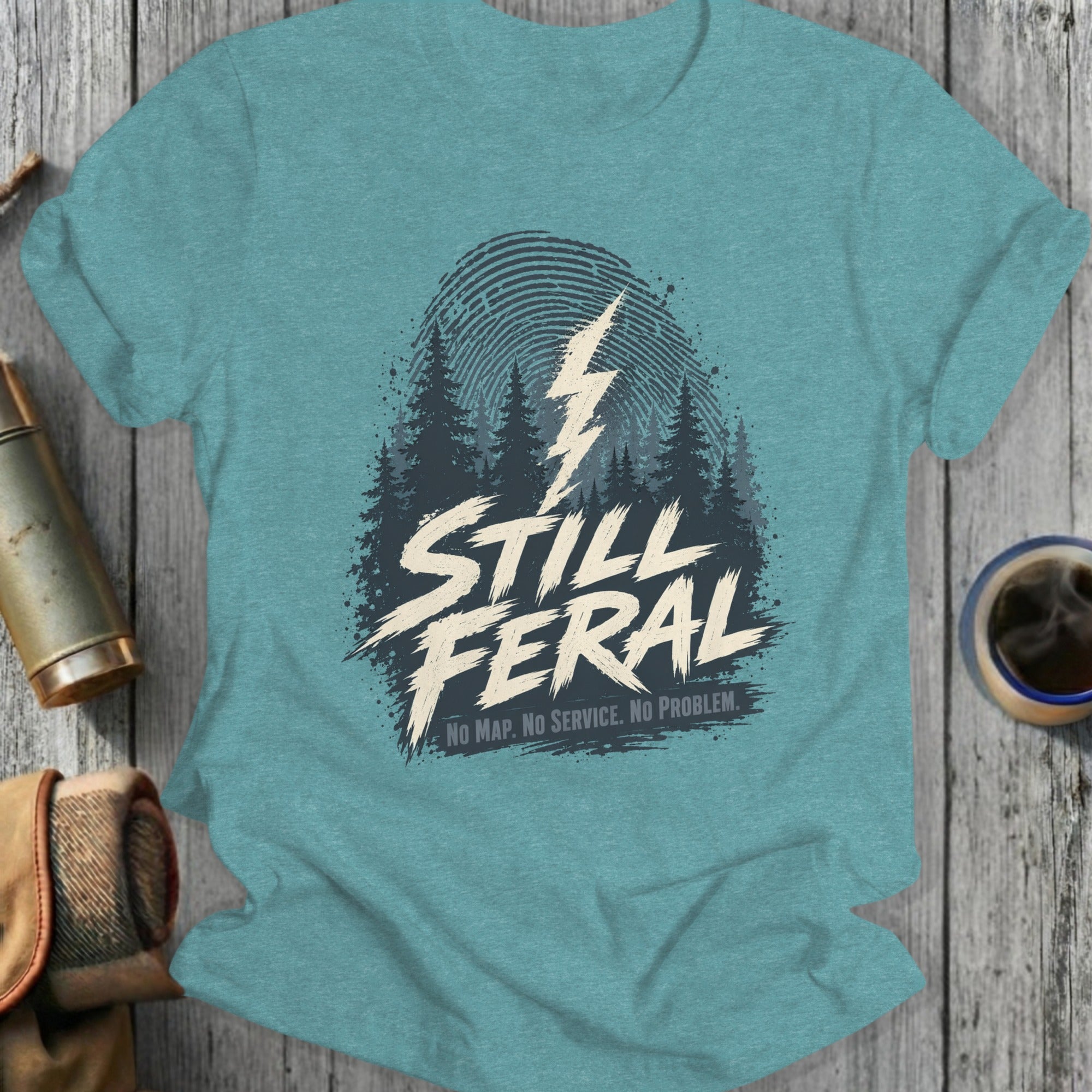 Teal t-shirt with "STILL FERAL" text, forest graphic, and lightning bolt.