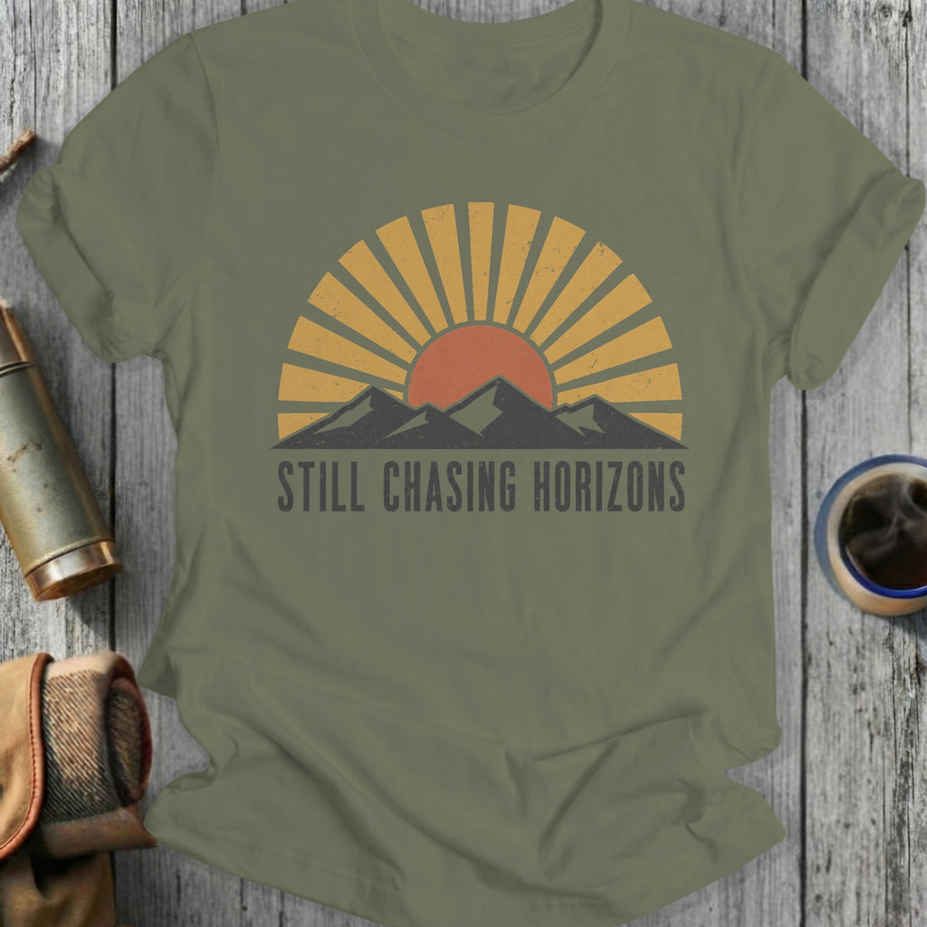 Olive green t-shirt with "STILL CHASING HORIZONS" text and sunset mountain graphic.