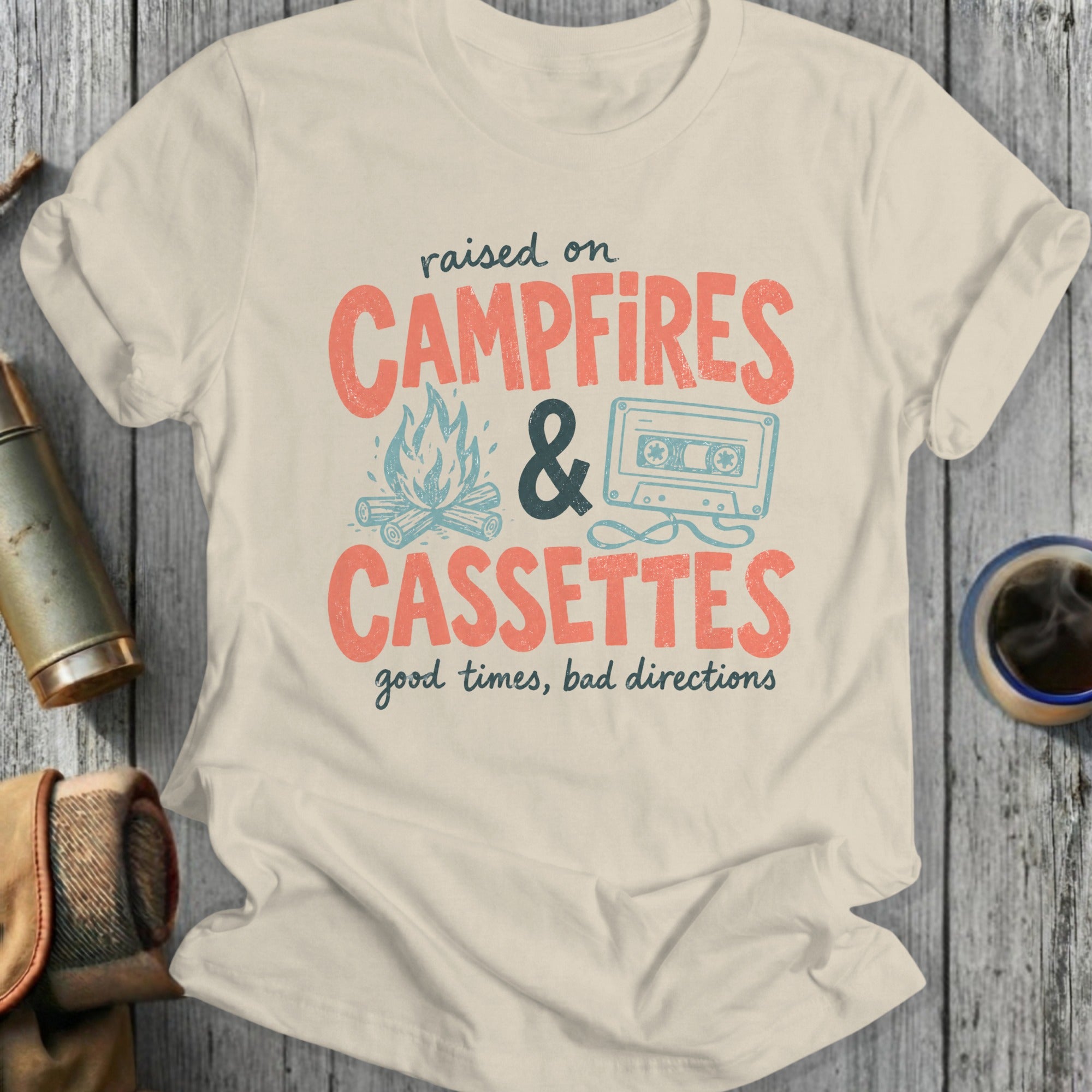Cream t-shirt with text "raised on CAMPFIRES & CASSETTES good times, bad directions".