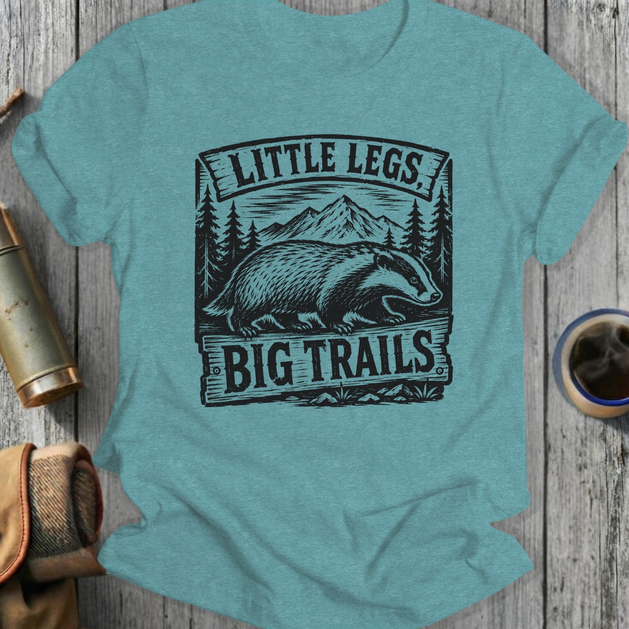 T-shirt with badger, mountains, trees, and text "LITTLE LEGS BIG TRAILS".