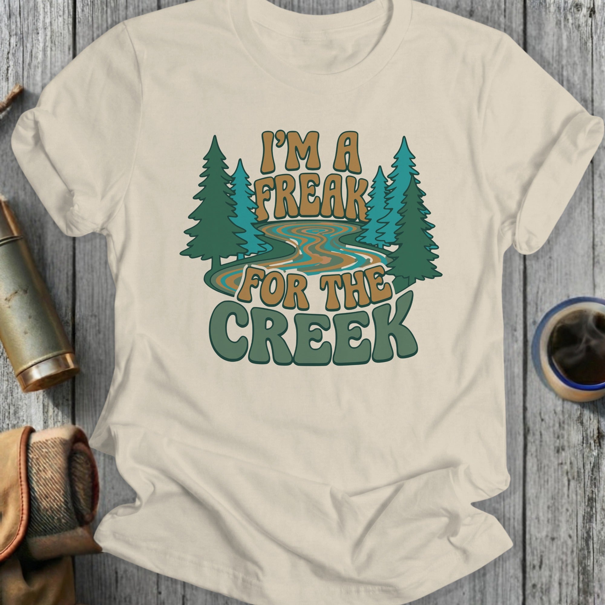 Cream t-shirt with "I'm a freak for the creek" text and stylized trees.